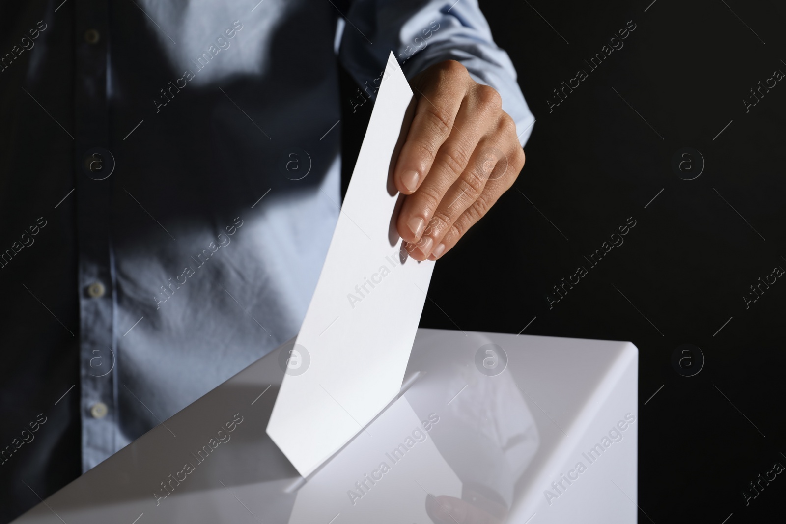 Photo of Man putting his vote into ballot box on black background, closeup