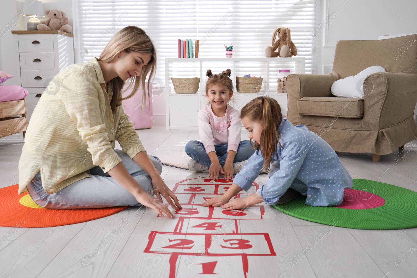 Photo of Mother and little girls taping sticker hopscotch on floor at home