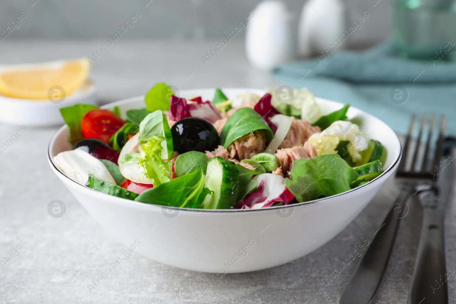 Photo of Bowl of delicious salad with canned tuna and vegetables served on light grey table