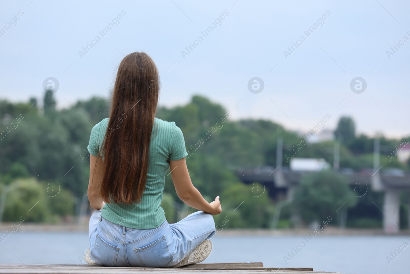 Photo of Teenage girl meditating near river, back view. Space for text