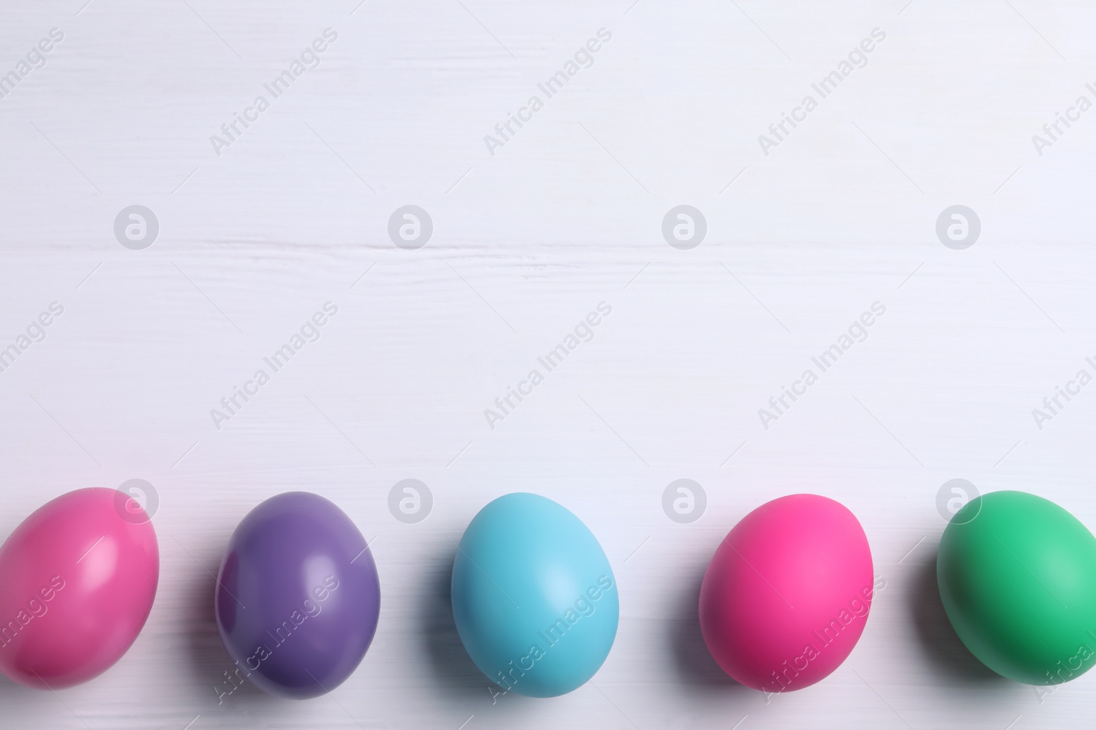 Photo of Colorful eggs on white wooden background, flat lay with space for text. Happy Easter