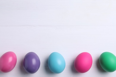 Photo of Colorful eggs on white wooden background, flat lay with space for text. Happy Easter