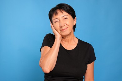 Photo of Senior woman suffering from ear pain on light blue background