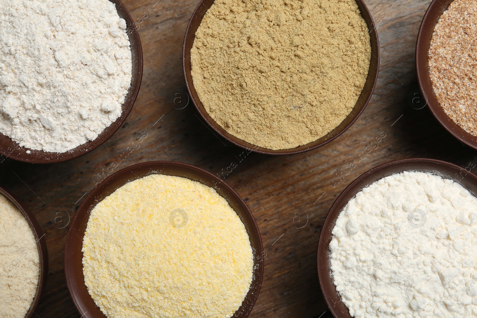 Photo of Bowls with different types of flour on wooden background, top view