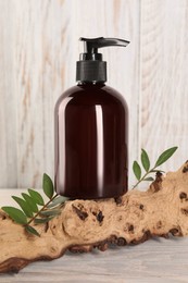 Photo of Shampoo bottle and tree branch on white wooden table