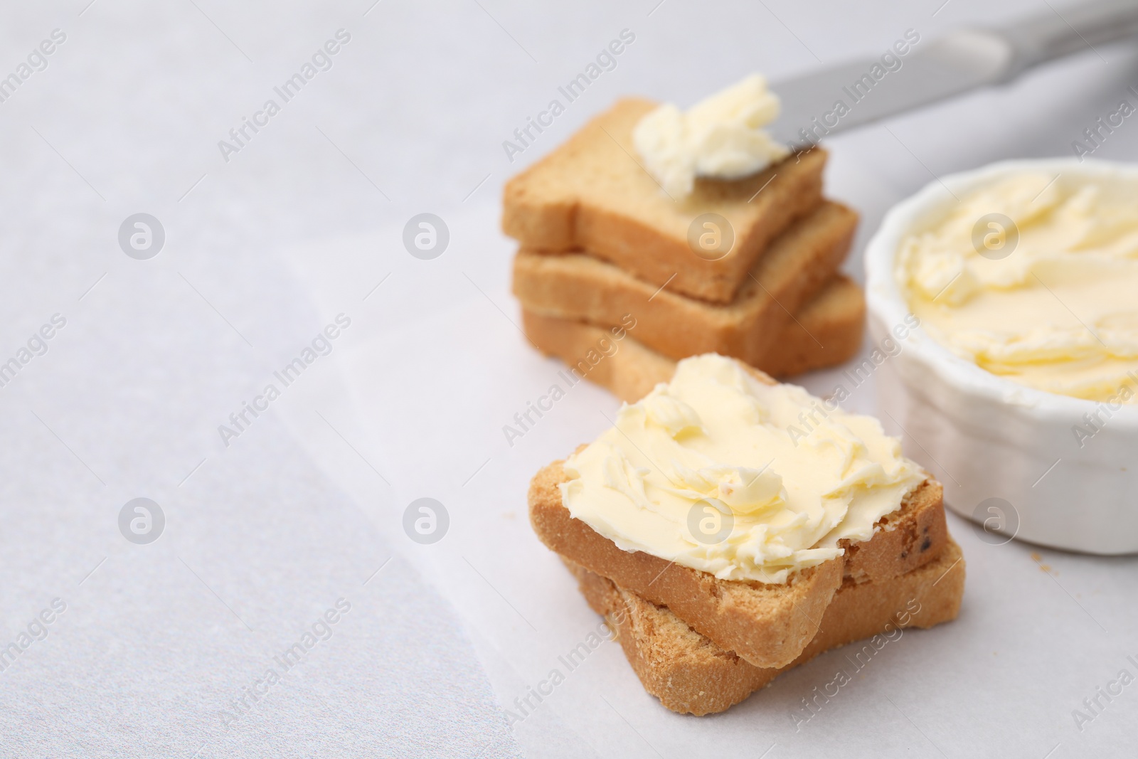 Photo of Slices of bread with tasty butter on light gray table, closeup. Space for text