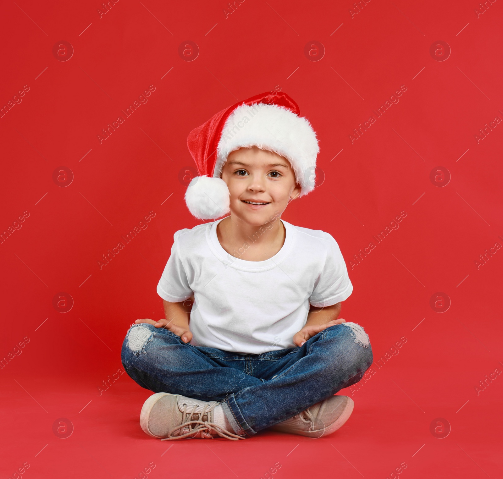 Photo of Cute little child wearing Santa hat on red background. Christmas holiday