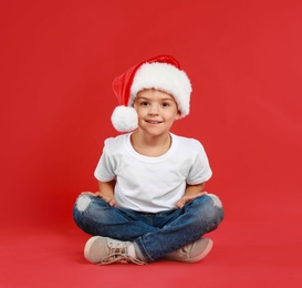 Cute little child wearing Santa hat on red background. Christmas holiday