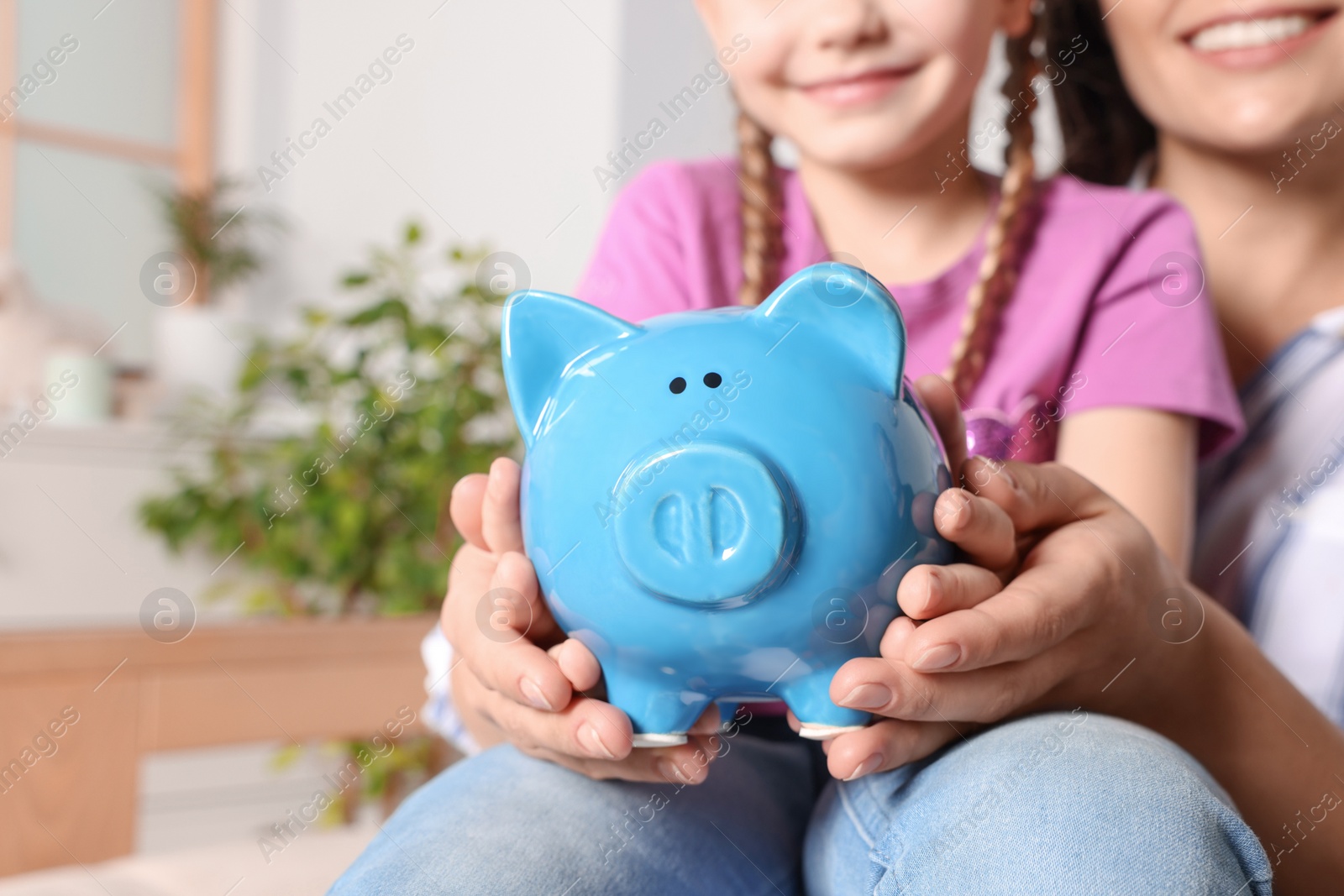 Photo of Closeup view of woman and her daughter with piggy bank at home