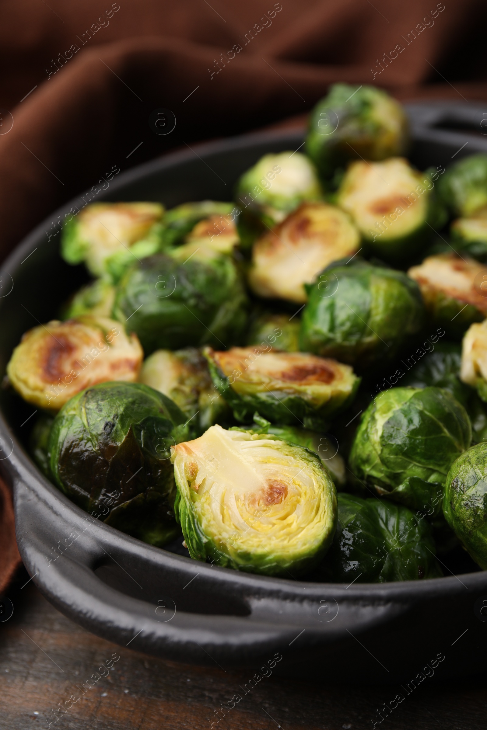 Photo of Delicious roasted Brussels sprouts in baking dish on wooden table, closeup