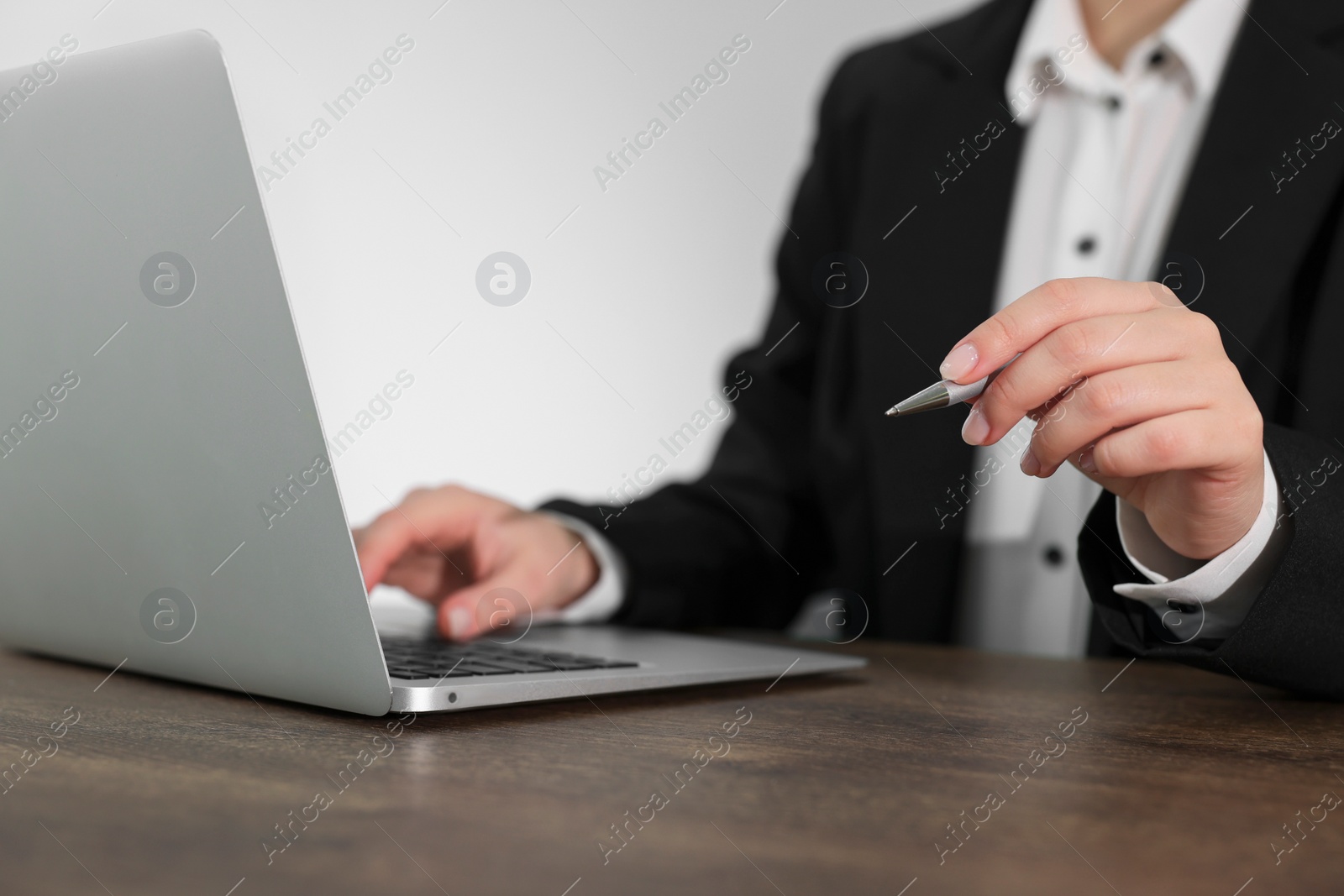 Photo of Woman with pen working on laptop at wooden table, closeup. Electronic document management