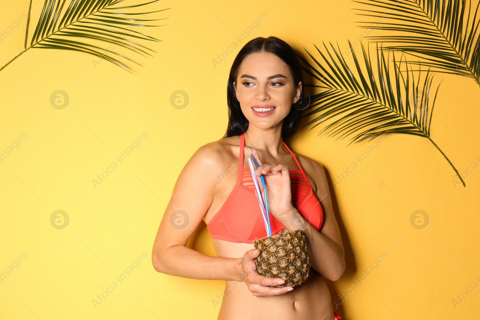 Photo of Beautiful young woman in stylish bikini with cocktail and tropical leaves on yellow background