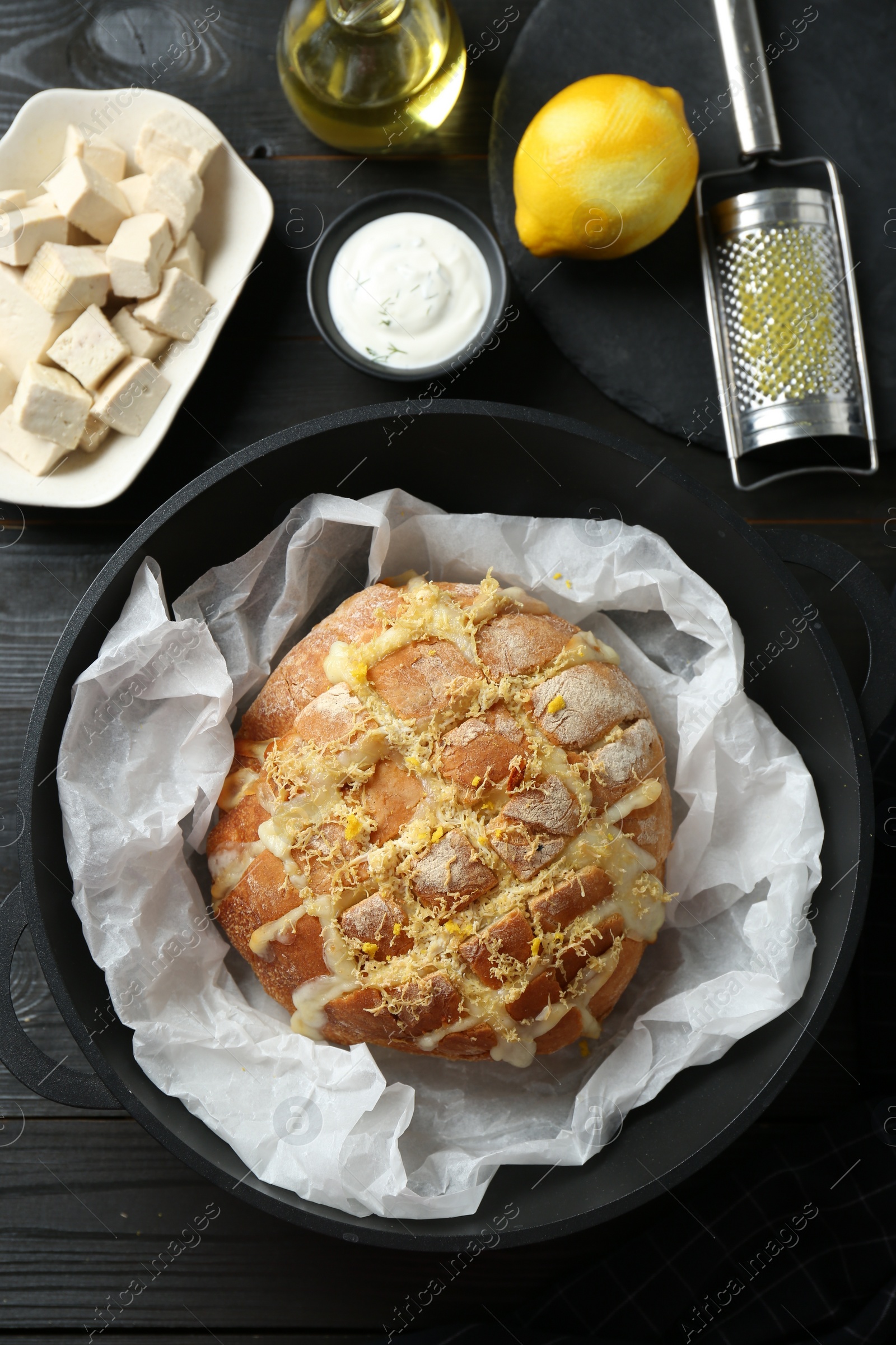 Photo of Freshly baked bread with tofu cheese and lemon zest served on black wooden table, flat lay