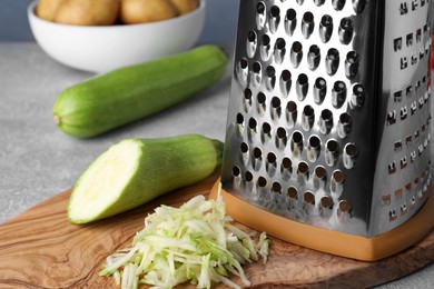 Grater and fresh zucchini on wooden board, closeup