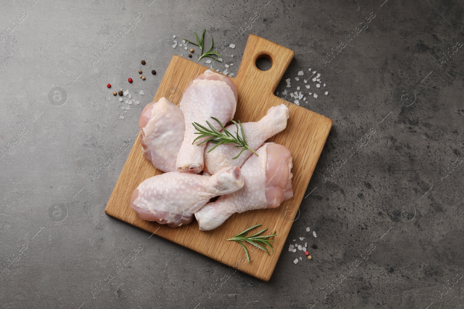 Photo of Raw chicken drumsticks with rosemary and spices on grey table, flat lay