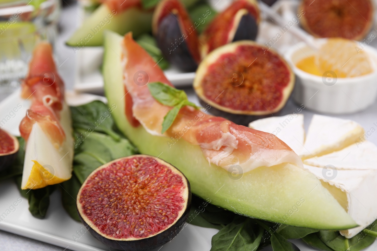 Photo of Tasty melon, jamon and figs served on white plate, closeup