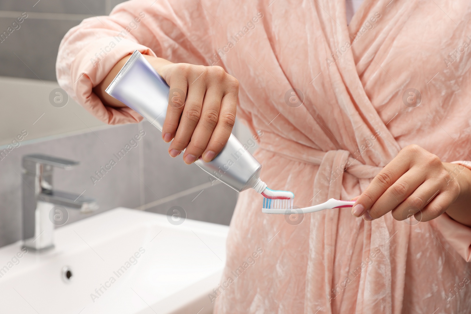 Photo of Woman applying toothpaste on brush in bathroom, closeup