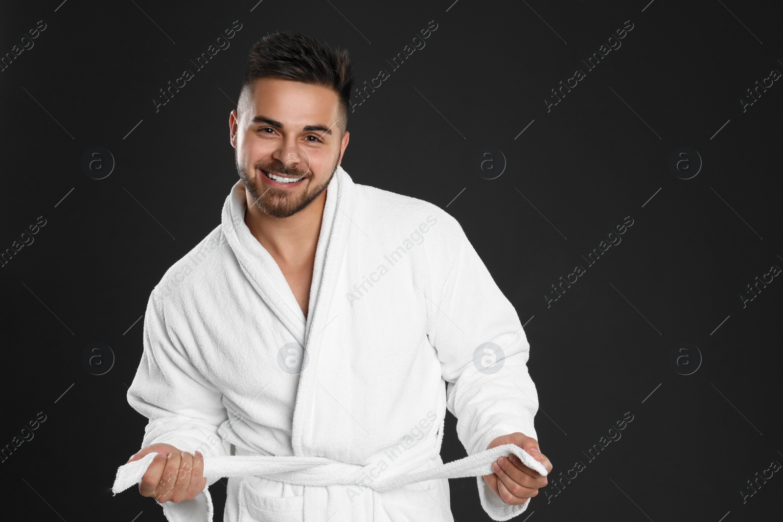 Photo of Happy young man in bathrobe on black background