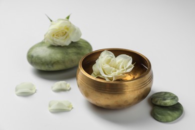 Photo of Tibetan singing bowl with water, beautiful rose flowers and spa stones on white background