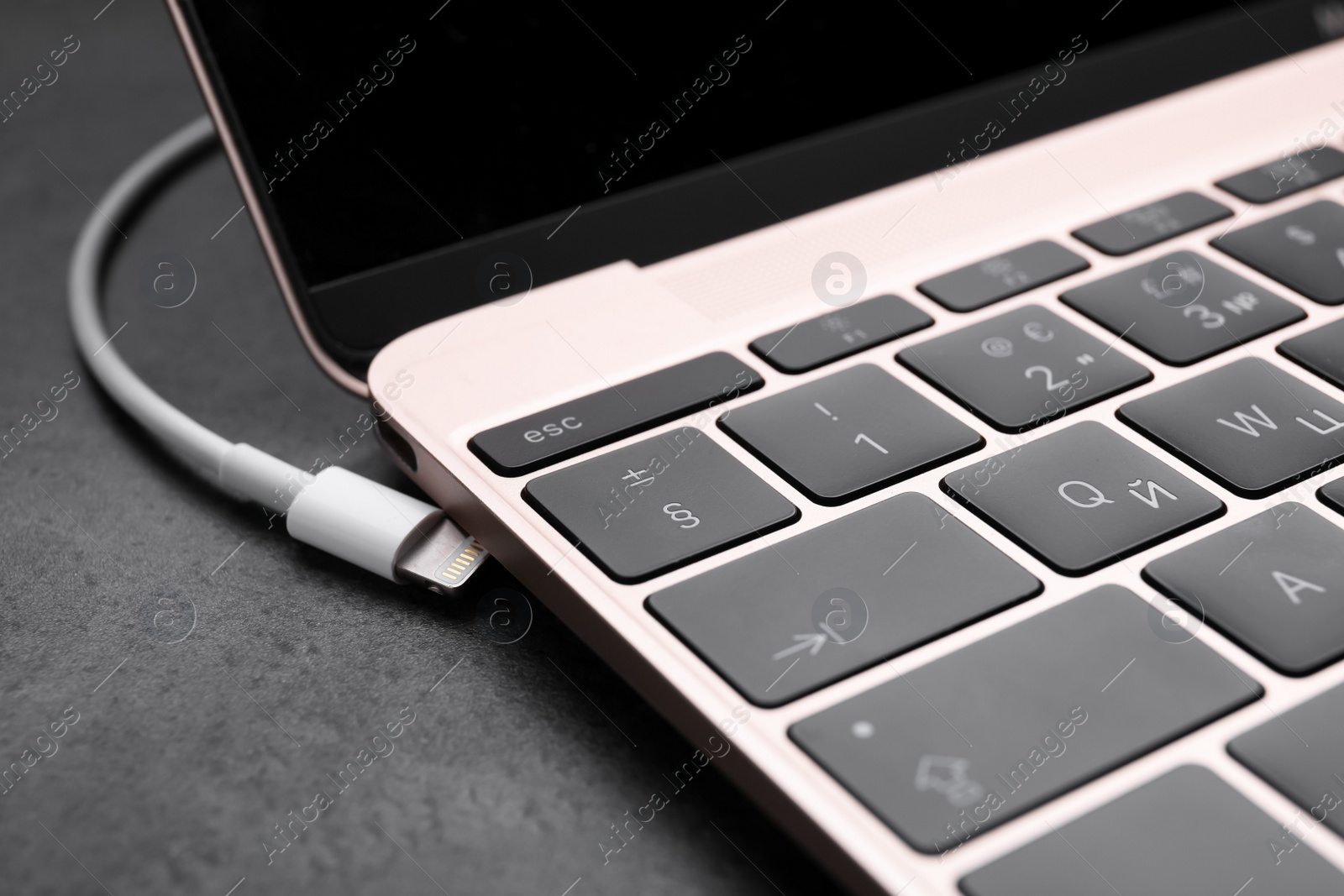 Photo of USB cable with lightning connector and laptop on black table, closeup