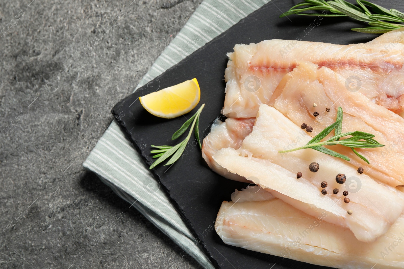 Photo of Pieces of raw cod fish, rosemary, peppercorns and lemon on grey table