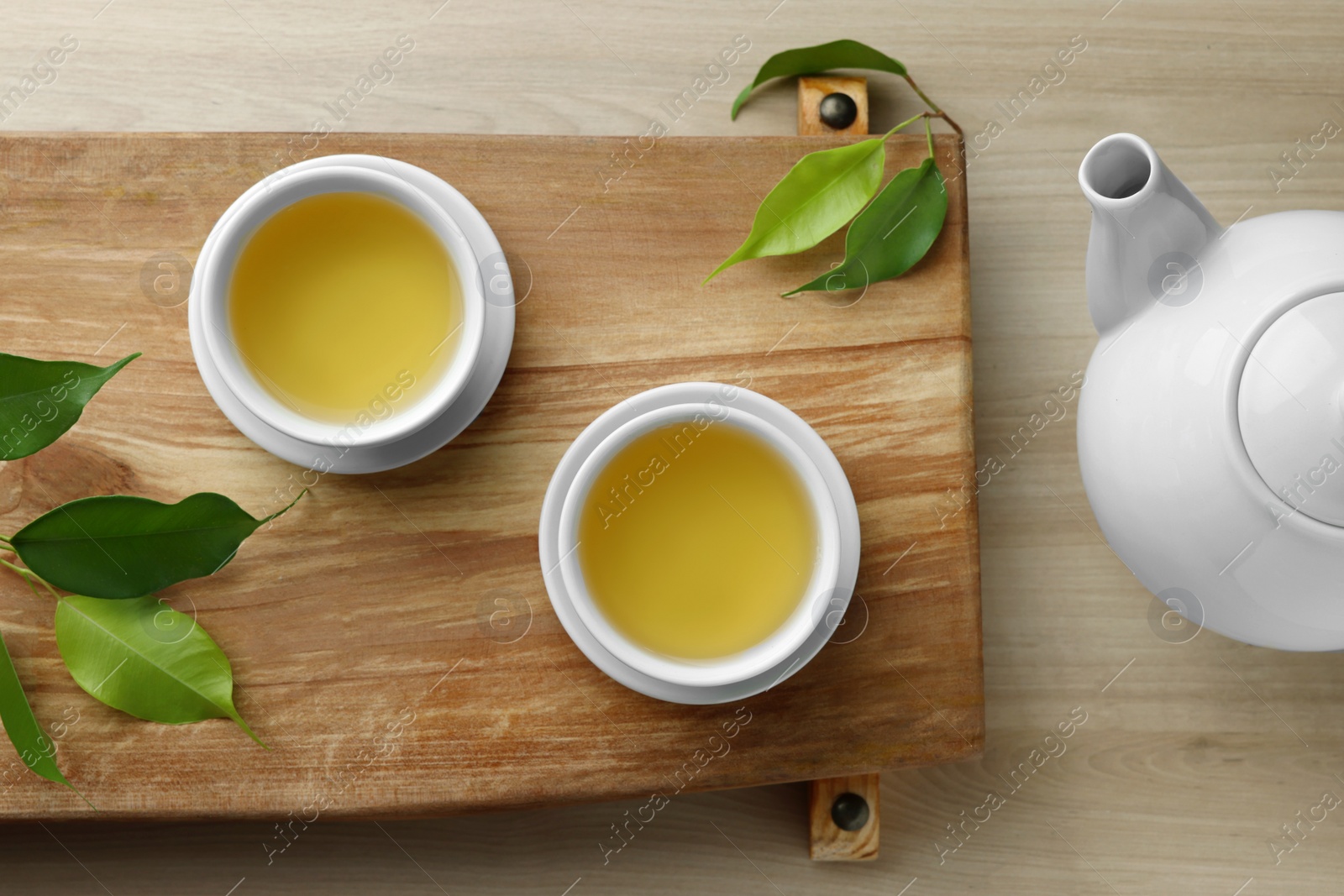Photo of Tray with white cups of green tea, leaves and teapot on wooden table, flat lay