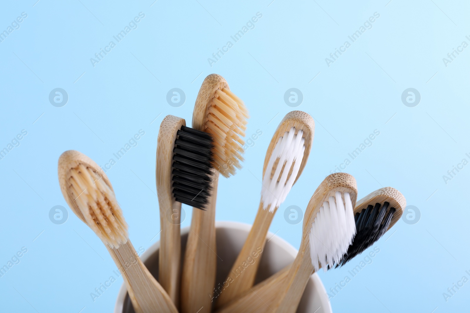 Photo of Bamboo toothbrushes in holder on light blue background, closeup