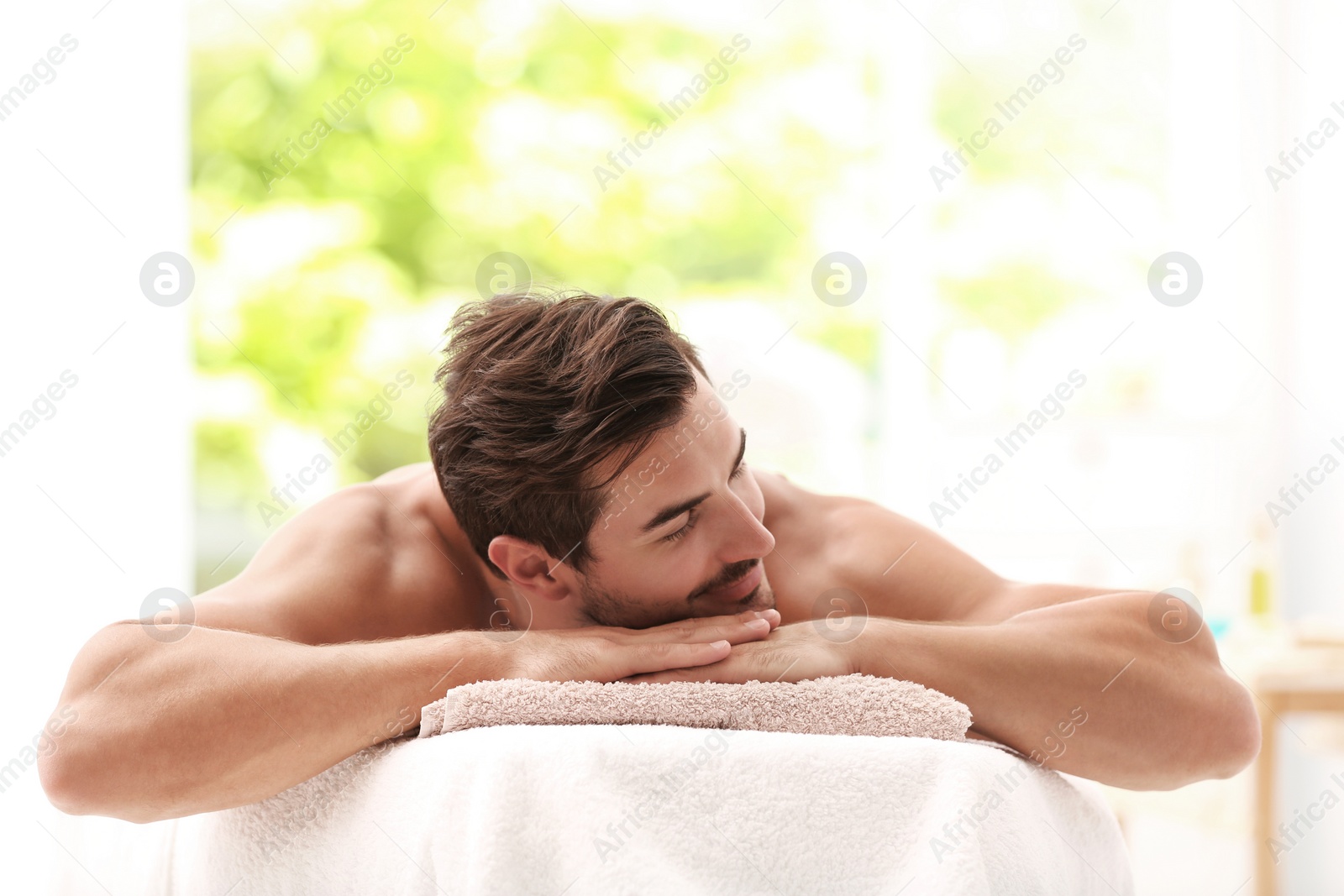 Photo of Handsome young man relaxing on massage table in spa salon, space for text