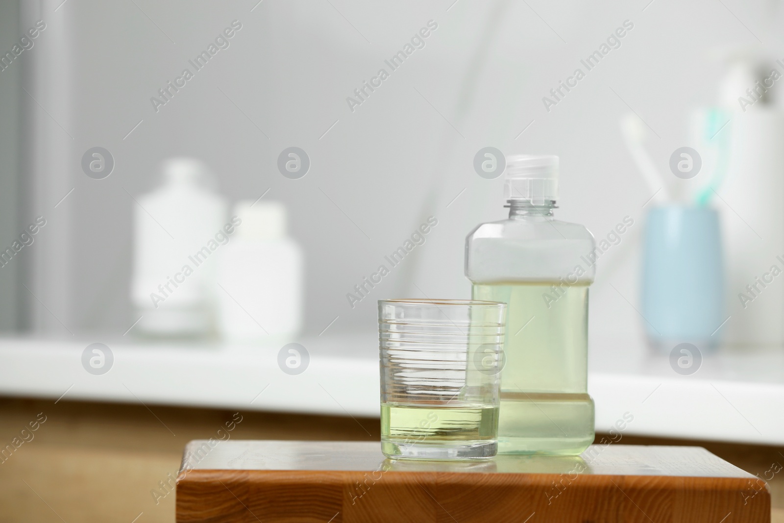 Photo of Bottle and glass with mouthwash on wooden table in bathroom, space for text