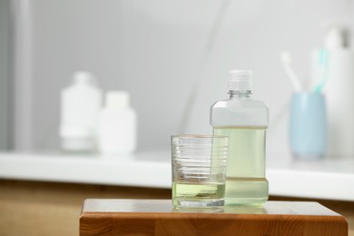 Bottle and glass with mouthwash on wooden table in bathroom, space for text