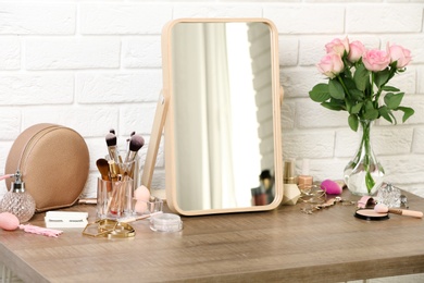 Photo of Different makeup products and accessories on dressing table in room interior