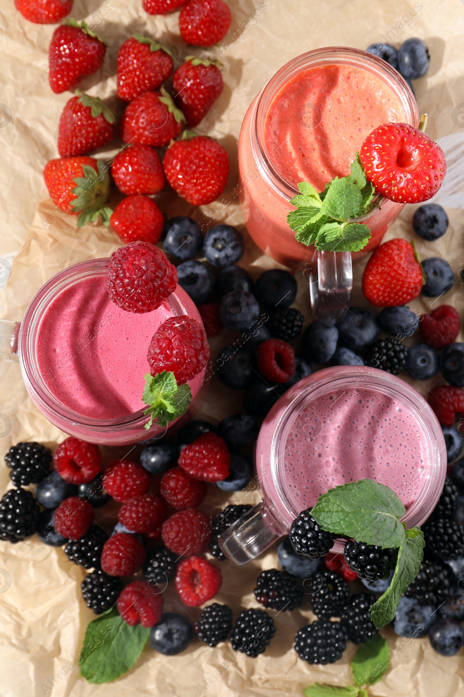 Photo of Mason jars of different berry smoothies and fresh ingredients on table, flat lay