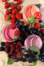 Mason jars of different berry smoothies and fresh ingredients on table, flat lay