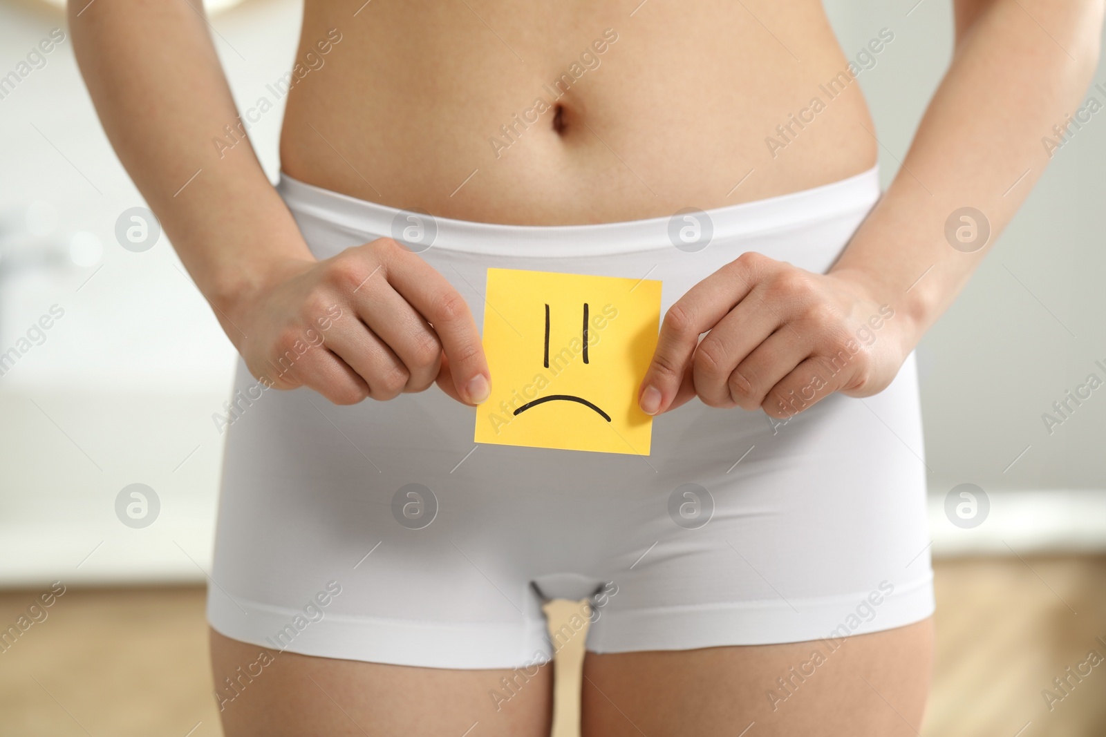 Photo of Cystitis. Woman holding sticky note with drawn sad face at home, closeup