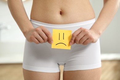 Cystitis. Woman holding sticky note with drawn sad face at home, closeup