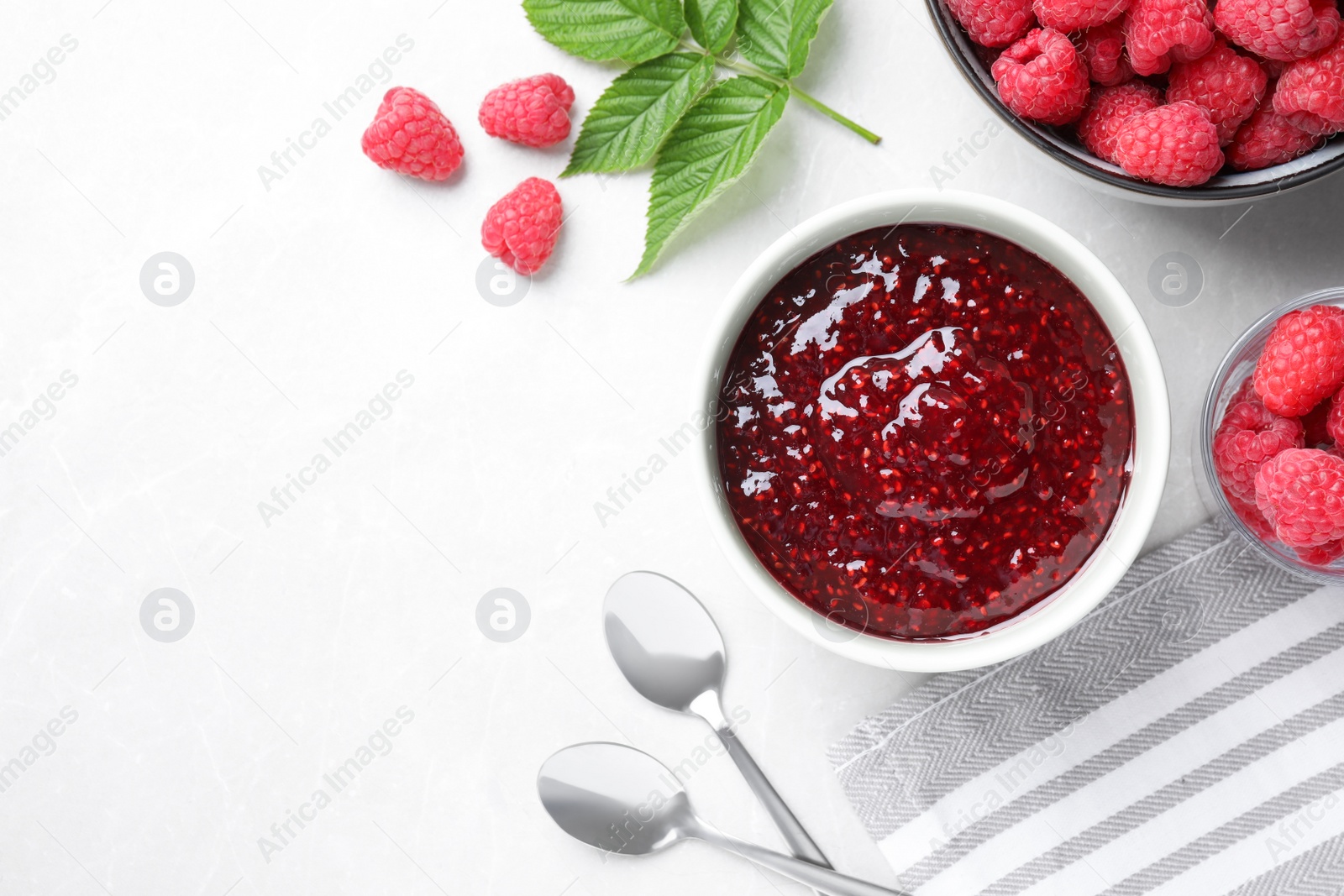 Photo of Delicious jam and fresh raspberries on white table, flat lay. Space for text