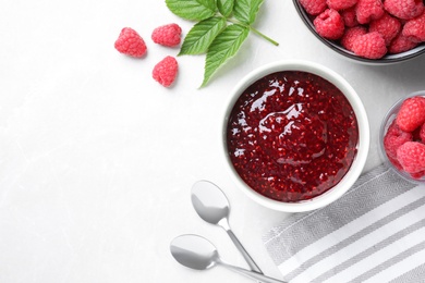 Delicious jam and fresh raspberries on white table, flat lay. Space for text