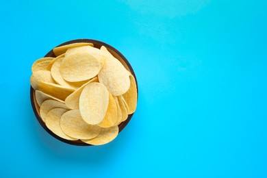 Photo of Bowl with delicious potato chips on light blue background, top view. Space for text