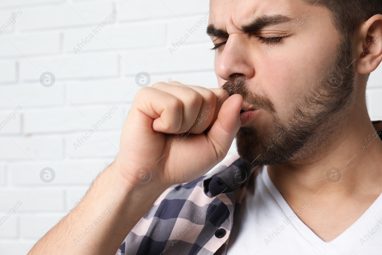 Photo of Handsome young man coughing near brick wall