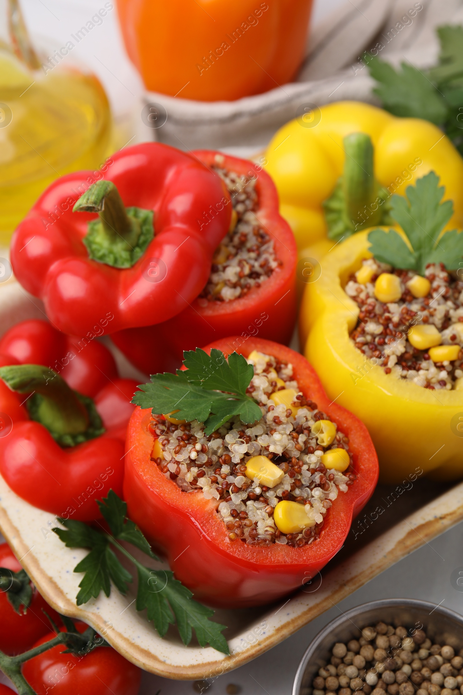 Photo of Quinoa stuffed bell peppers in baking dish, parsley, tomatoes and peppercorns on white table, closeup