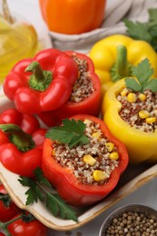 Photo of Quinoa stuffed bell peppers in baking dish, parsley, tomatoes and peppercorns on white table, closeup