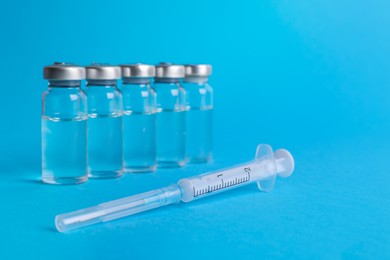 Disposable syringe with needle and vials on light blue background