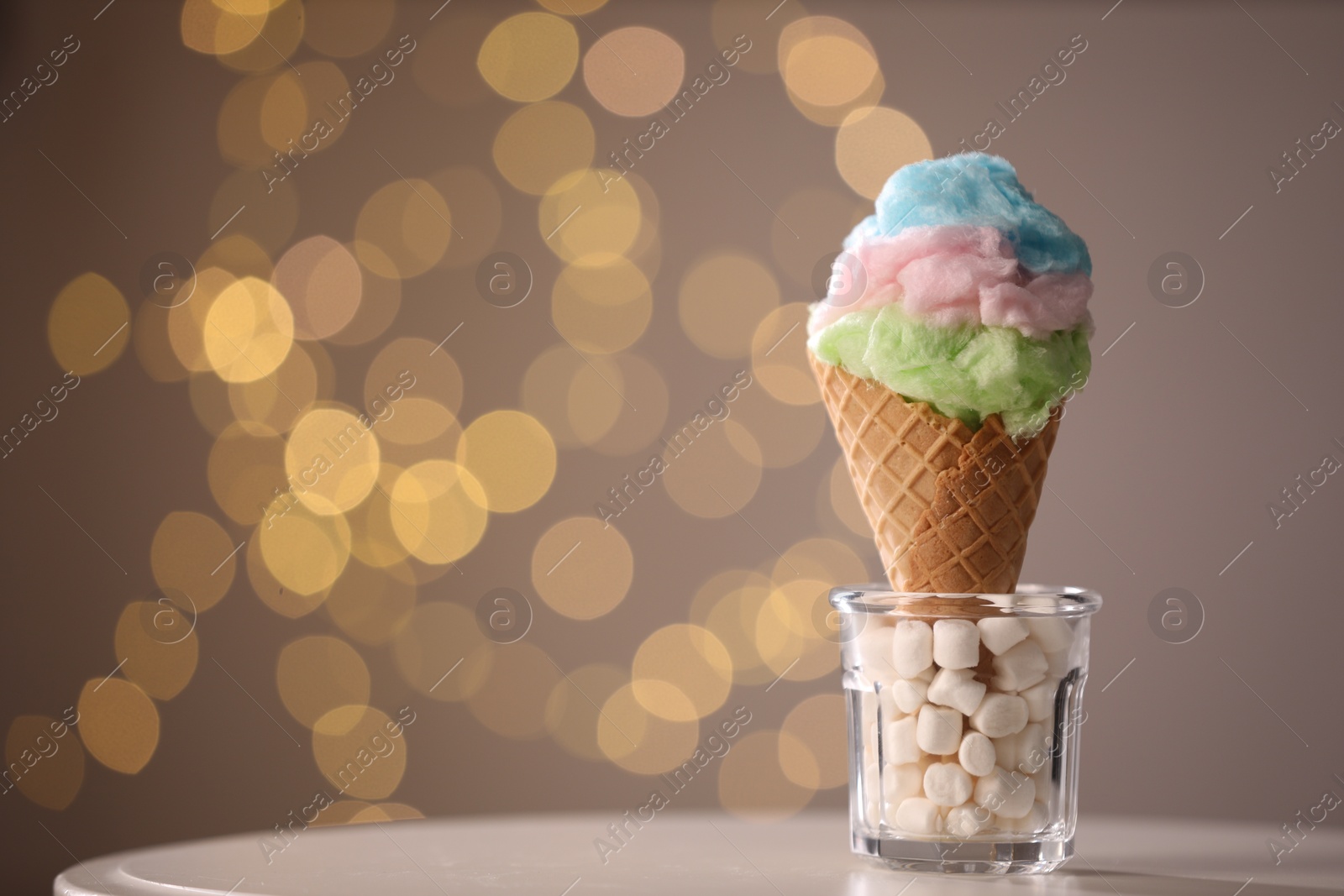 Photo of Sweet cotton candy in waffle cone on table against blurred lights, closeup. Space for text