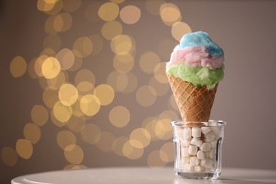 Sweet cotton candy in waffle cone on table against blurred lights, closeup. Space for text