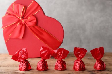 Delicious chocolate candies in red wrappers and heart shaped box on wooden table