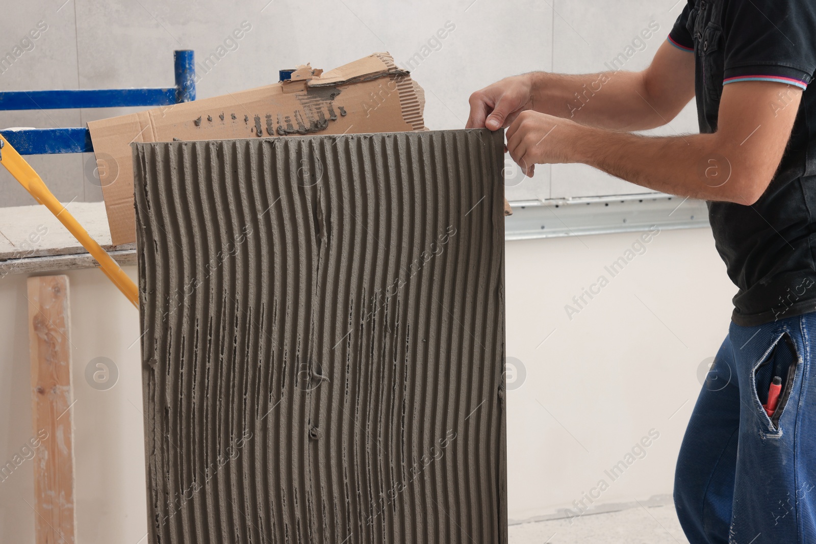 Photo of Worker holding tile with adhesive mix indoors, closeup