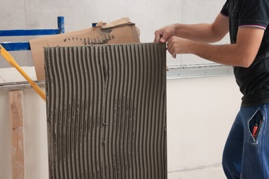 Photo of Worker holding tile with adhesive mix indoors, closeup