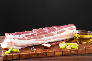Photo of Piece of raw pork belly, green chili pepper, oil and salt on wooden table, closeup