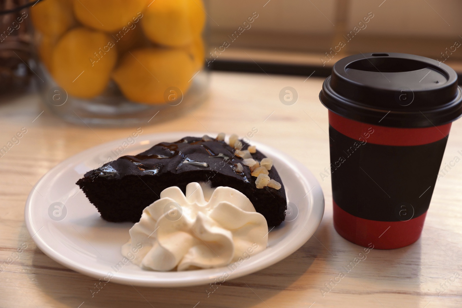 Photo of Tasty coffee in takeaway paper cup and dessert on wooden table indoors