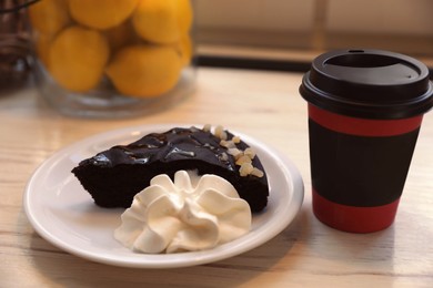 Photo of Tasty coffee in takeaway paper cup and dessert on wooden table indoors